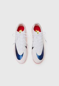 White athletic shoes with a textured surface, navy blue accents, and a red insole. Features white laces and a yellow logo on the tongue.