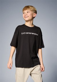 Črna bombažna majica s postopno zavitimi rokavi, z belim logotipom "EA7 EMPORIO ARMANI" na prsih. Gladka tekstura, sproščen kroj.