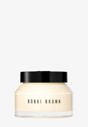 Bobbi Brown cream in a transparent jar with a black lid, showing pale beige product inside and brand name on the front.