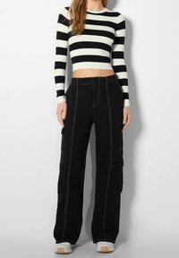 Pantalon cargo noir avec surpiqûres blanches, coupe ample, poches latérales, associé à un haut à manches longues rayé noir et blanc, court.