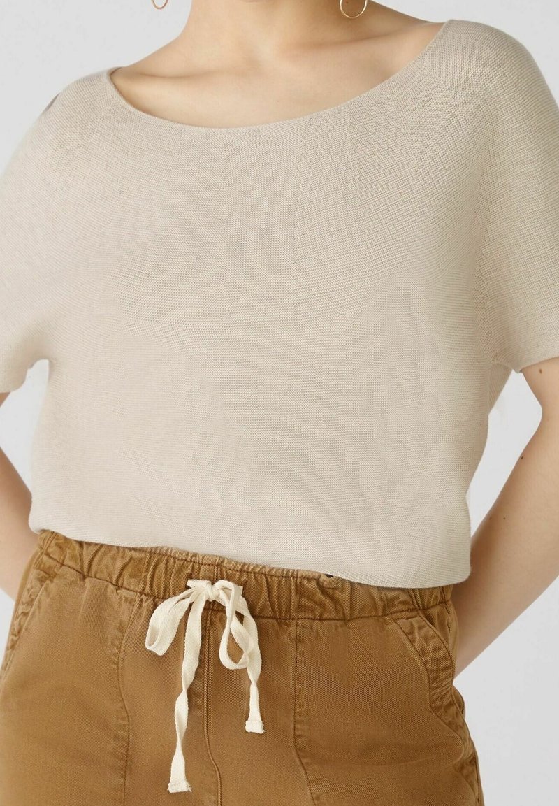 Haut en tricot beige avec un décolleté bateau oversized. Associé à un short marron à taille élastique avec cordon de serrage et détails de poches.