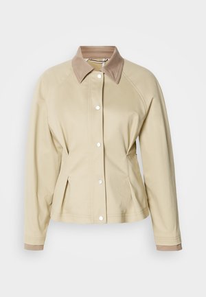 Jachetă bej cu un guler contrastant de nuanță maro, închidere cu capse și mâneci raglan. Are un design ajustat și o textură netedă.