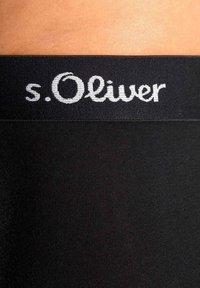 Musta vyötärönauha, jossa on valkoinen s.Oliver-logo, sileä ja joustava pinta; näkyvät ompeleet ylä- ja alareunoissa.
