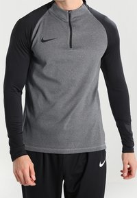 Camiseta de manga larga de Nike con diseño de media cremallera. Cuerpo gris con mangas negras, tejido texturizado y un pequeño logo en el pecho.