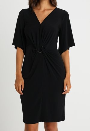 Schwarzes knielanges Kleid mit V-Ausschnitt, kurzen weiten Ärmeln und einem vorne gerafften Detail, das an der Taille durch zwei silberne Ringe zusammengehalten wird.