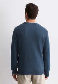 Blauer Strickpullover mit Rippstruktur und Rundhalsausschnitt. Lange Ärmel und ein gerippter Saum. Der Stoff wirkt weich und dick.