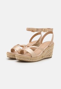 Beige wedge sandals with a braided jute sole, featuring a metallic strap design, ankle buckle, and smooth texture on the footbed.