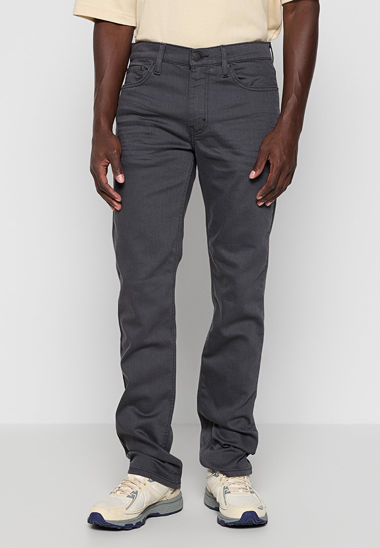 Donkergrijze recht gesneden jeans met vijf zakken, riemlussen en een gladde textuur, gecombineerd met lichtgekleurde sportschoenen.