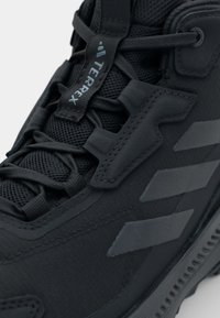 Black athletic shoe featuring a textured upper, mesh panels, and distinct angular detailing. Includes contrasting gray accents and lacing system.