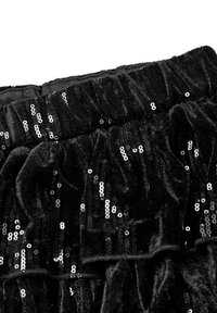 Černý sametový materiál s rozptýlenými lesklými černými flitry a elastickým pasem, zobrazující texturu a jiskření na detailním záběru.