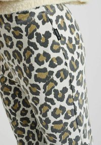 Luipaardprint broek met een witte achtergrond en zwarte en bruine vlekken, slim fit ontwerp en een klein merklabel op de zijnaad.