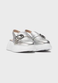 Zapatos slingback metálicos en plata con suela blanca gruesa, que presentan un detalle de hebilla y un material superior texturizado.