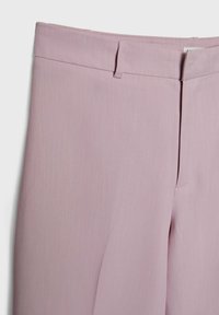Gros plan d’un pantalon sur mesure rose clair avec passants de ceinture et fermeture éclair à l’avant sur fond blanc.