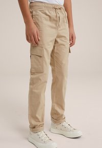 Beige cargo kalhoty vyrobené z bavlněné směsi, s bočními kapsami, elastickým pasem a zúženou nohavicí. V kombinaci s bílými vysokými teniskami.