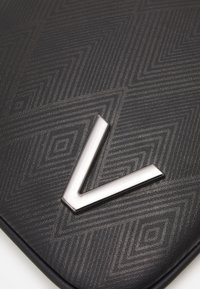 Svart texturerad läderpås med ett geometriskt mönster och en framträdande silvermetallic "V"-detalj på framsidan.
