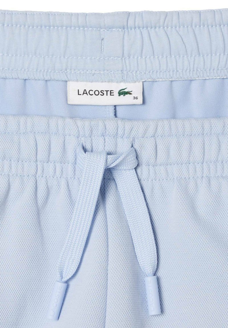 Pantalones cortos de Lacoste en azul claro con cintura elástica, cordones y una tela texturizada que presenta una pequeña etiqueta con el logo.