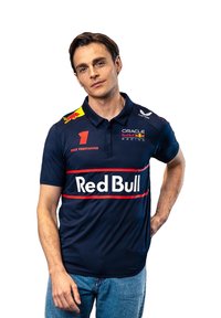 Koszulka polo w kolorze granatowym z logo Red Bull Racing, czerwonymi paskami i żółtymi akcentami. Wykonana z gładkiego materiału, z kołnierzykiem i krótkimi rękawami.