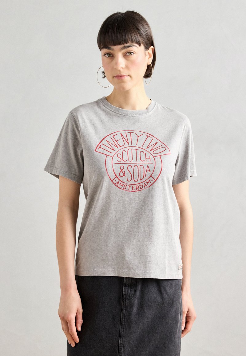 Graues Baumwoll-T-Shirt mit kurzen Ärmeln. Auf der Vorderseite befindet sich ein rotes rundes Logo mit dem Text "TWENTY TWO SCOTCH & SODA AMSTERDAM" in der Mitte.