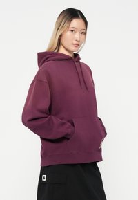 Felpa bordeaux con tasca frontale, cappuccio con coulisse e polsini a coste. Il tessuto sembra morbido e confortevole, adatto per un abbigliamento casual.