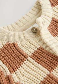Strickpullover mit abwechselnden creme- und terrakottafarbigen Schachbrettmustern, geripptem Kragen und einer braunen Knopfakzentuierung.