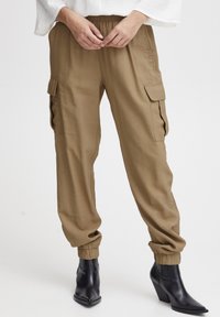 Kaki cargobyxor med resårmidja, sidofickor och manschetter, tillsammans med spetsiga svarta ankelboots.