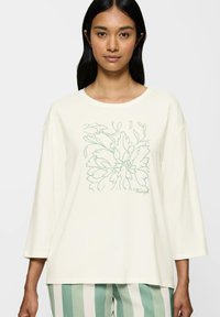 Kremowy, dług rękawowy top z kwiatowym rysunkiem konturowym w jasnej zieleni. Luźny krój z okrągłym dekoltem i miękką fakturą.