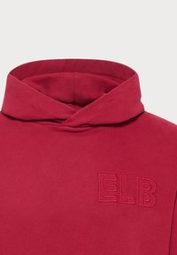 Piros kapucnis pulóver, puha textúrával, hajtott nyakkal és hímzett "ELB" részlettel az elülső részen. Egyszerű dizájn és laza stílus.