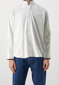 Weißes Langarmhemd mit hohem Kragen und schwarzen Akzenten am Kragen und an den Manschetten. Hergestellt aus glattem Stoff, bietet es eine lockere Passform.