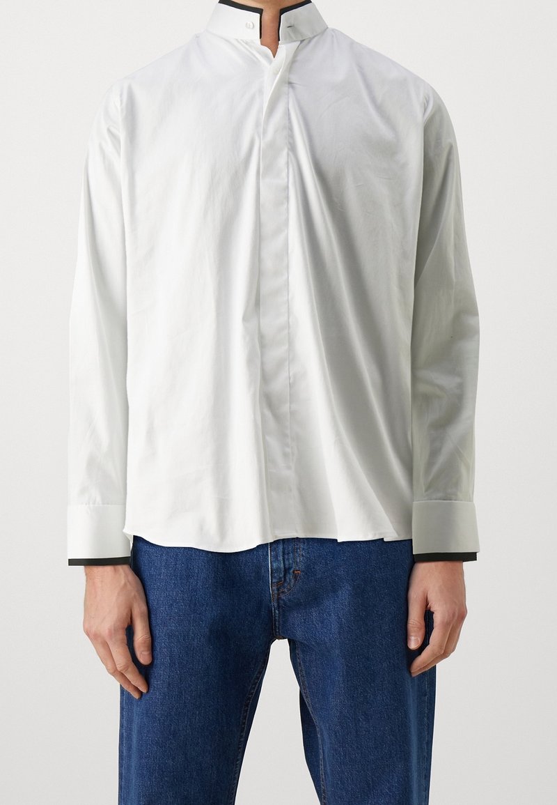 Weißes Langarmhemd mit hohem Kragen und schwarzen Akzenten am Kragen und an den Manschetten. Hergestellt aus glattem Stoff, bietet es eine lockere Passform.