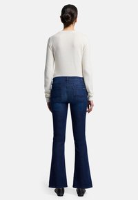 Maglione chiaro in crema, aderente, a maniche lunghe; jeans blu scuro a palazzo, a vita alta, con due tasche posteriori e dettagli di cucitura sottili.
