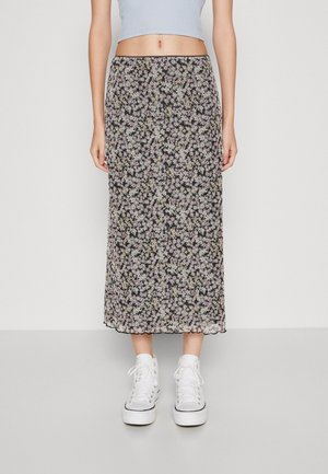 Kvinde iført en sort midi-nederdel med et lille hvidt blomstermønster, hvide højtoppede sneakers og en cropped lyseblå top.