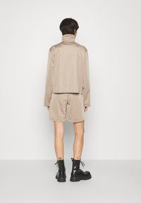 Beige sportkläderset bestående av en långärmad topp med krage och matchande shorts. Strukturväv. Svarta snörboots med grova sulor.