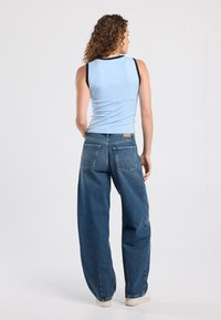 Light blue sleeveless top with black trim, paired with loose-fitting blue denim jeans featuring two back pockets and a label detail.