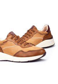 Zapatillas de cuero marrón con un acabado suave, costuras en contraste y una suela blanca gruesa. Cuenta con seis ojales para los cordones y un cuello acolchado.