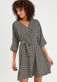 Robe noir et blanche avec un motif en vagues, décolleté en V, manches trois-quarts, taille cintrée et jupe fluide. Texture de tissu douce.
