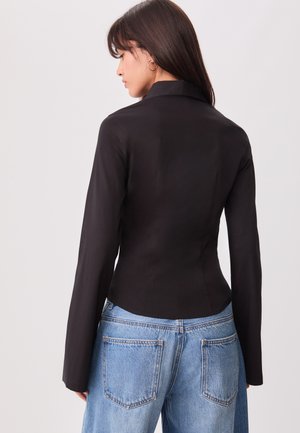 Black fitted jacket with a smooth texture and long sleeves, paired with light blue oversized denim jeans featuring back pockets.
