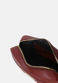 Clutch rossa in pelle con superficie testurizzata. Chiusura con zip dorata e rivestimento interno nero. Presenta una parte superiore aperta e una forma piatta e strutturata.