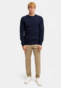 Laivastonsininen ribbineulepusero pyöreällä kaula-aukolla, yhdistetty khakinvärisiin housuihin ja valkoisiin tennareihin. Puserossa on pitkät hihat ja istuva malli.