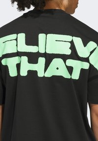 Czarna koszulka z dużym, teksturowanym mintowym napisem "WIERZ W TO" na plecach; krótki rękaw i standardowy krój.