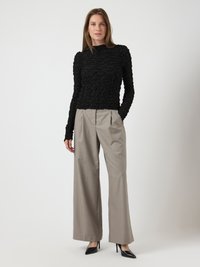 Maglietta nera a maniche lunghe con un collo alto, abbinata a pantaloni larghi grigio chiaro e tacchi a punta neri.