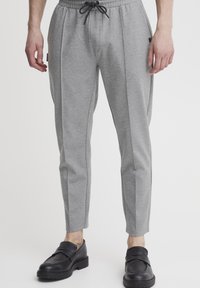 Grå, tætsiddende sweatpants med elastisk talje og snørelukning; sidelægstriber; glat tekstur; båret med sorte loafers.