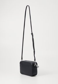 Svart skinn crossbody-veske med rektangulær form, glidelås, justerbar stropp og minimalistisk design. Glatt tekstur, ingen synlige mønstre.