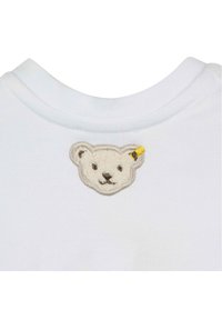 Cuello de camisa de algodón blanco que presenta un rostro de oso texturizado y bordado con un acento amarillo. Cosido a máquina en colores neutros.