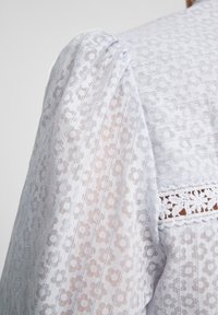 Blusa azzurro chiaro con tessuto traslucido a fiori, righe testurizzate e dettagli in pizzo intricati lungo il collo.