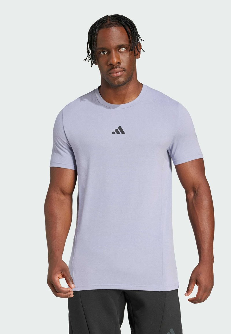 Camiseta deportiva de color púrpura claro, hecha de tela suave, con mangas cortas y un sutil logo negro de Adidas en el pecho.