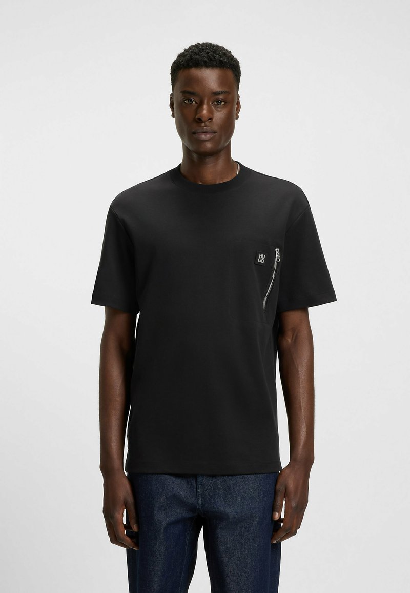 T-shirt nera a maniche corte con scollatura rotonda, dotata di tasca con zipper sul petto e un accento logo testurizzato. Tessuto liscio, vestibilità comoda.