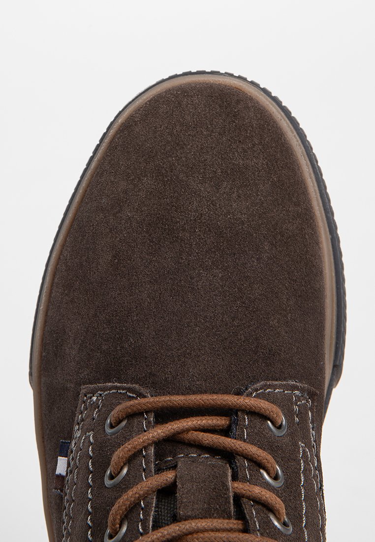 Scarpa in suede marrone con punta rotonda, lacci marroni e dettagli di cucitura bianca. Suola in gomma e accento del logo sottile vicino ai lacci.