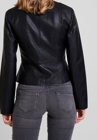 Schwarze Lederjacke mit tailliertem Schnitt, glatter Textur und Nahtdetails. Getragen über grauer Jeans mit klassischem Fünf-Taschen-Stil.