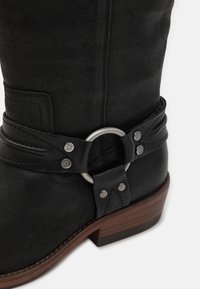 Black leather western-style boot with a rounded toe, featuring a decorative belt and silver circular buckle, and a stacked wooden heel.