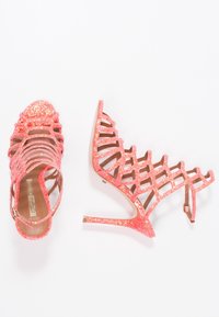 Rosa glittriga högklackade sandaler med ett korsande mönster, öppen tå och smal stilettklack, med ett bakre vristband.